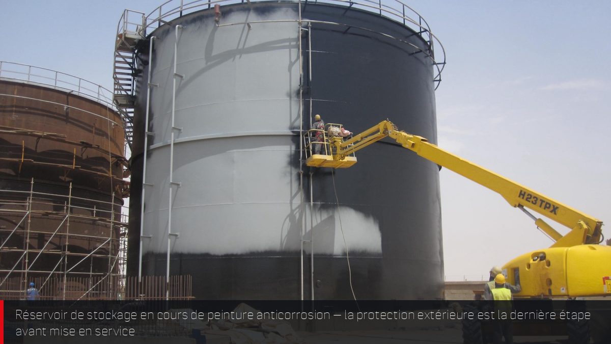 Grand réservoir de stockage métallique en cours de peinture anticorrosion par nacelle